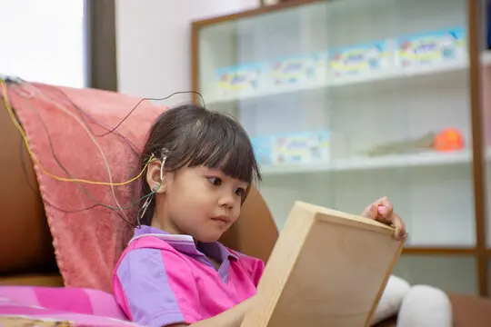 A little girl is wearing a hearing aid and is doing a neurofeedback exam. Making EEG electrodes. A little girl is wearing a hearing aid and is doing a neurofeedback exam. Making EEG electrodes.