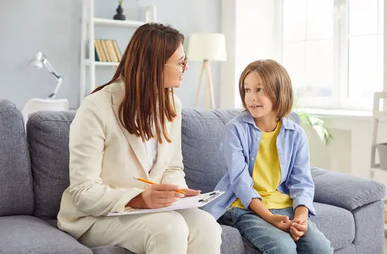 Portrait of a friendly young female psychologist woman doctor talking with her child girl patient sitting on sofa in office during therapy session. Psychotherapy and kids mental health concept. Portrait of a friendly young female psychologist woman doctor talking with her child girl patient sitting on sofa in office during therapy session. Psychotherapy and kids mental health concept.